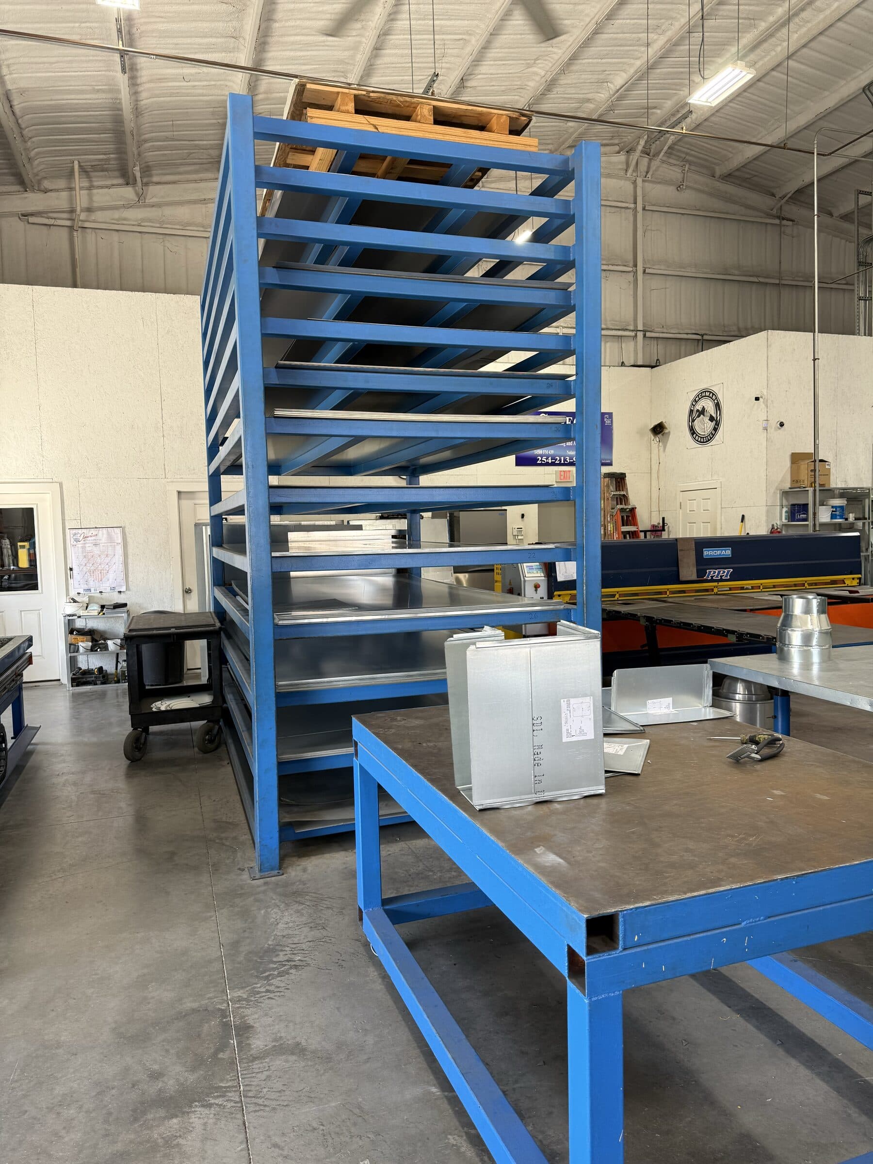 Sheet metal components organized on a material rack beside a fabrication table