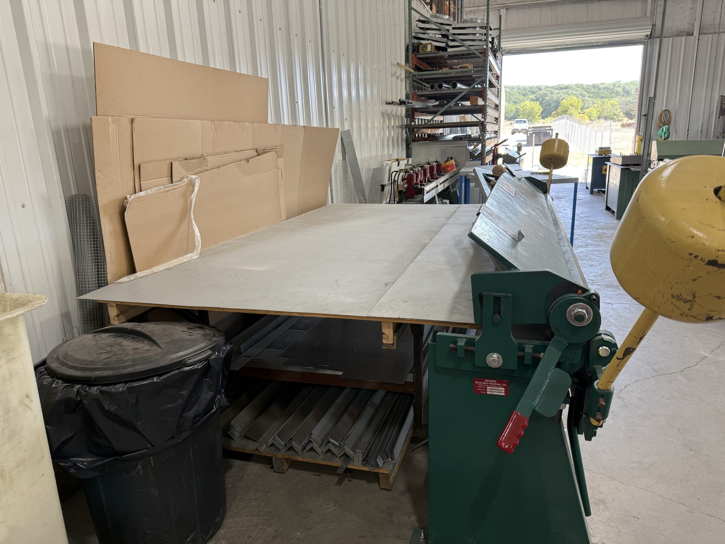 Sheet material positioned across a shop worktable beside forming equipment